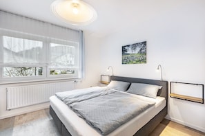 Een moderne slaapkamer met een groot bed, nachtkastjes, een radiator en een raam met uitzicht.