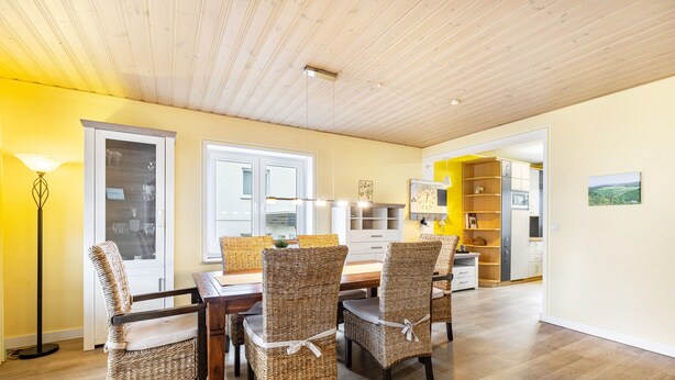 A dining area with wicker chairs, a wooden table, and a modern kitchen in the background.