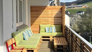 A balcony with a wooden deck, a green sofa with cushions, and a red chair.