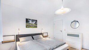A bedroom with a bed, bedside tables, a mirror, a door, and a wall-mounted picture.