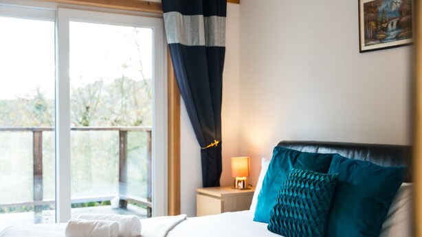 A hotel room with a bed, a nightstand with a lamp, and a view of the outdoors. - Westwood in Oban Town Centre (Argyll and Bute Council)