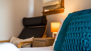 A hotel room with a bed, a bedside table, a lamp, a chair, and a wall-mounted shelf. - Westwood in Oban Town Centre (Argyll and Bute Council)