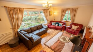 A living room with a brown leather sofa, a red leather sofa, and a red armchair. There is a wooden floor, a patterned rug, and a chandelier. - Westwood in Oban Town Centre (Argyll and Bute Council)