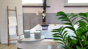 A spa area with a massage table, candles, a towel rack, and a potted plant.
