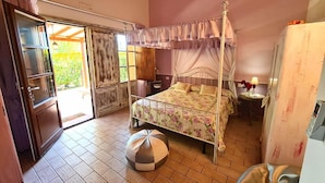 Une chambre à coucher avec un lit à baldaquin, un petit pouf rond, une table de chevet, une lampe et une armoire.