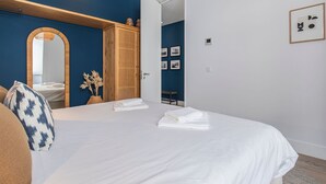 A hotel room with a large bed, a wooden wardrobe, a mirror, and a small table with a chair. - Ando Living - Abrantes Flats - 13 (Lisbon)