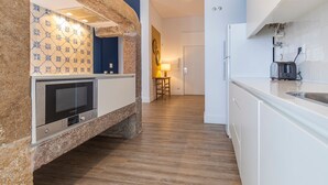 A modern kitchen with a built-in microwave, a coffee maker, and a stone accent wall. - Ando Living - Abrantes Flats - 23 (Lisbon)