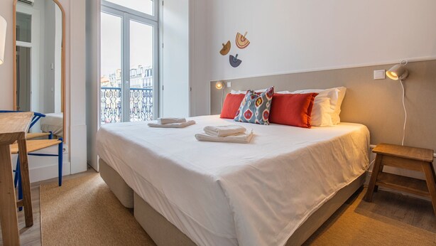 A neatly made bed with white linens, a small bedside table, and a chair with a blue frame. - Ando Living - Abrantes Flats - 23 (Lisbon)
