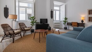 Una sala de estar moderna con un sofá azul, sillas de mimbre, una mesita de madera y plantas en macetas.