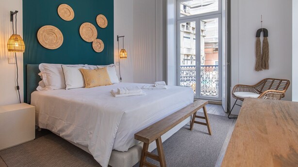 Ein Schlafzimmer mit einem Bett, Nachttischen, einer Bank und Blick auf den Balkon.