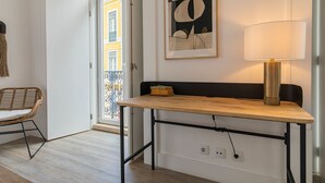 Ein Zimmer mit einem Holztisch, einem schwarzen Stuhl, einer Lampe und einem Bilderrahmen mit einem abstrakten Gemälde.