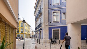 Eine schmale Straße mit Gebäuden, die blaue und gelbe Fassaden haben, ein Roller, der am Gehweg steht, und ein Fußgänger, der vom Kameraobjektiv wegggeht.
