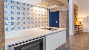 A kitchen with a white countertop, blue star-patterned backsplash, and a stone accent wall. - Ando Living - Abrantes Flats - 13 (Lisbon)