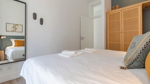 Un lit bien fait, avec du linge de lit blanc et des serviettes pliées, une armoire en bois et un miroir au mur.