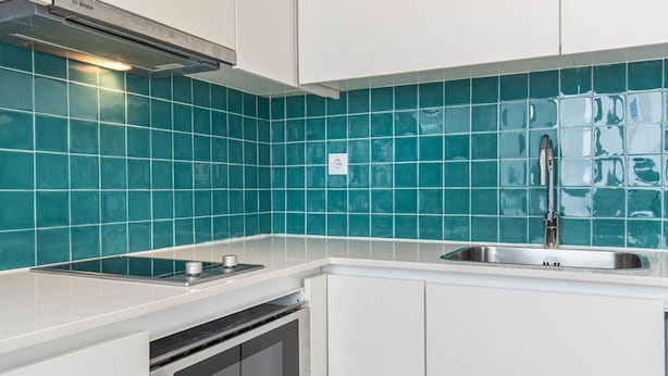 Une cuisine avec des carreaux de couleur turquoise, des appareils en acier inoxydable et des meubles blancs.