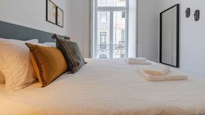 A hotel room with a bed, pillows, a window, and a door. - Ando Living - Abrantes Flats - 31 (Lisbon)