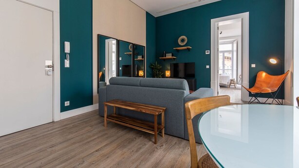 Un salon moderne avec des murs de couleur turquoise, un canapé gris, un banc en bois et une table en verre.