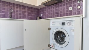 Une petite buanderie moderne, dotée d’un lave-linge Bosch, d’un évier et de murs recouverts de carreaux violets.