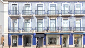 Un edificio con fachadas de azulejos azules, varios balcones con barandillas de hierro forjado y escaparates con señalización.