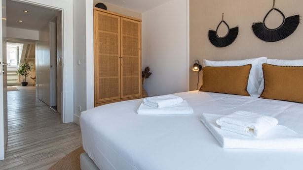Habitación de hotel con una cama grande, dos almohadas, una mesita de noche, una lámpara de pared y un armario de madera.