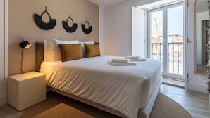 Una cama bien hecha con sábanas blancas y dos almohadas marrones, una lámpara de noche y un adorno en la pared.