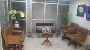 Un vestíbulo con dos sofás de cuero, una mesita de madera con un arreglo floral, un sofá negro y una planta en maceta.
