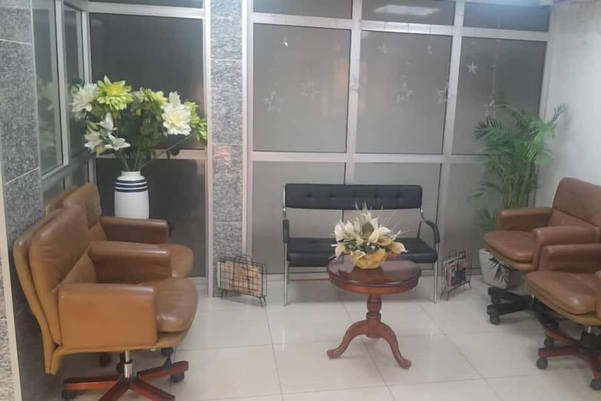 Ένας χώρος υποδοχής με δύο δερμάτινους καναπέδες, ένα μικρό ξύλινο τραπέζι με μια σύνθεση από λουλούδια, έναν μαύρο καναπέ και ένα φυτό σε γλάστρα.