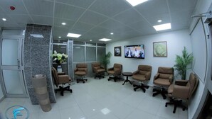 Un área de recepción con techo alto, iluminación empotrada y un conjunto de sillas marrones y una pequeña mesa.