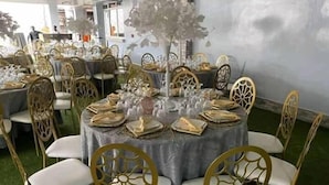 Un salón de banquetes con mesas redondas cubiertas con manteles blancos, sillas doradas y centros de mesa florales.