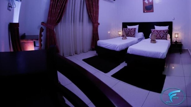 Habitación de hotel con dos camas, un escritorio y una silla. Se observa un equipo de aire acondicionado en la pared y un cuadro sobre la cama.