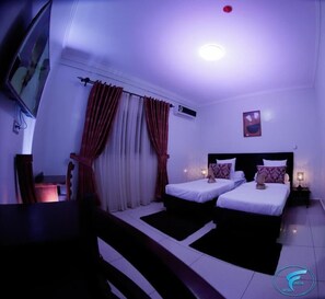 A hotel room with two beds, a desk, and a chair. There is an air conditioning unit on the wall and a painting above the bed. - HOTEL FREESIA  (Yaoundé)