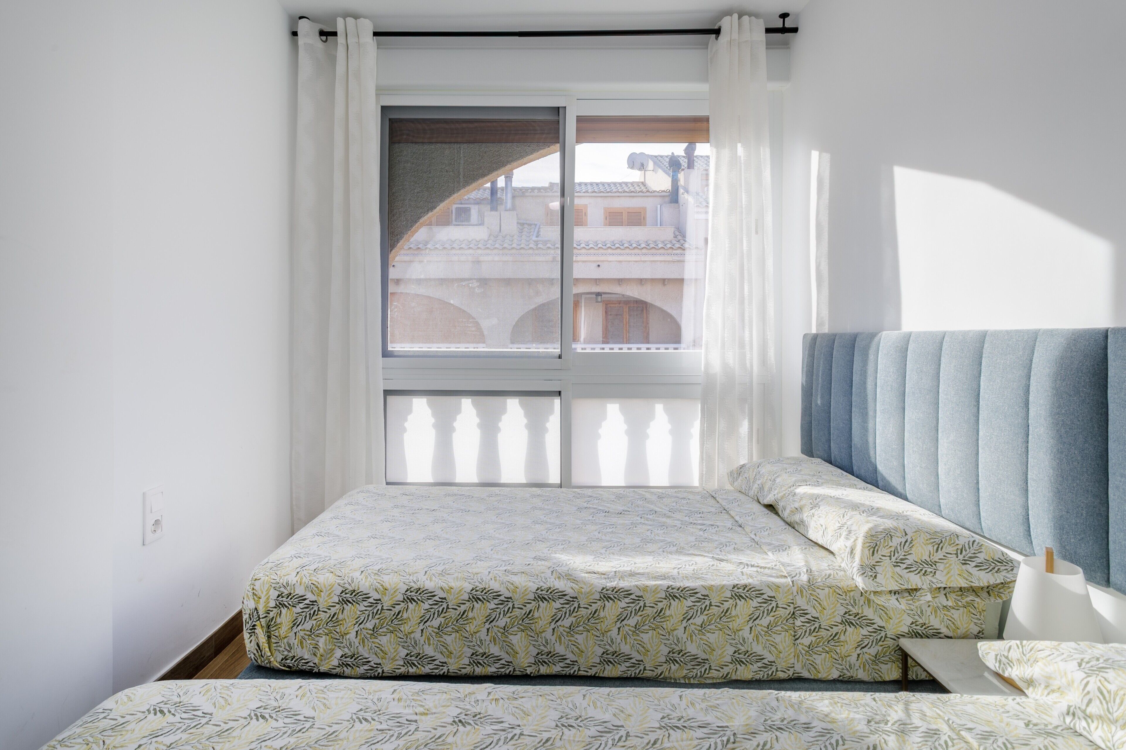 Une chambre à coucher avec un lit, une fenêtre avec des rideaux et une vue sur les bâtiments à l’extérieur.