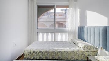Une chambre à coucher avec un lit, une fenêtre avec des rideaux et une vue sur les bâtiments à l’extérieur.