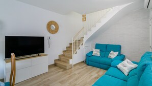 Ett modernt vardagsrum med en platt-TV, en trappa och en soffa i turkos.
