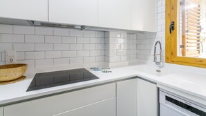 Ett kök med vita kakelplattor, en trävåg, en svart induktionshäll och en diskmaskin.