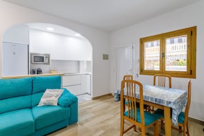 En kompakt opholdsstue med tekøkken, spiseplads med bord og stole, samt en sofa.