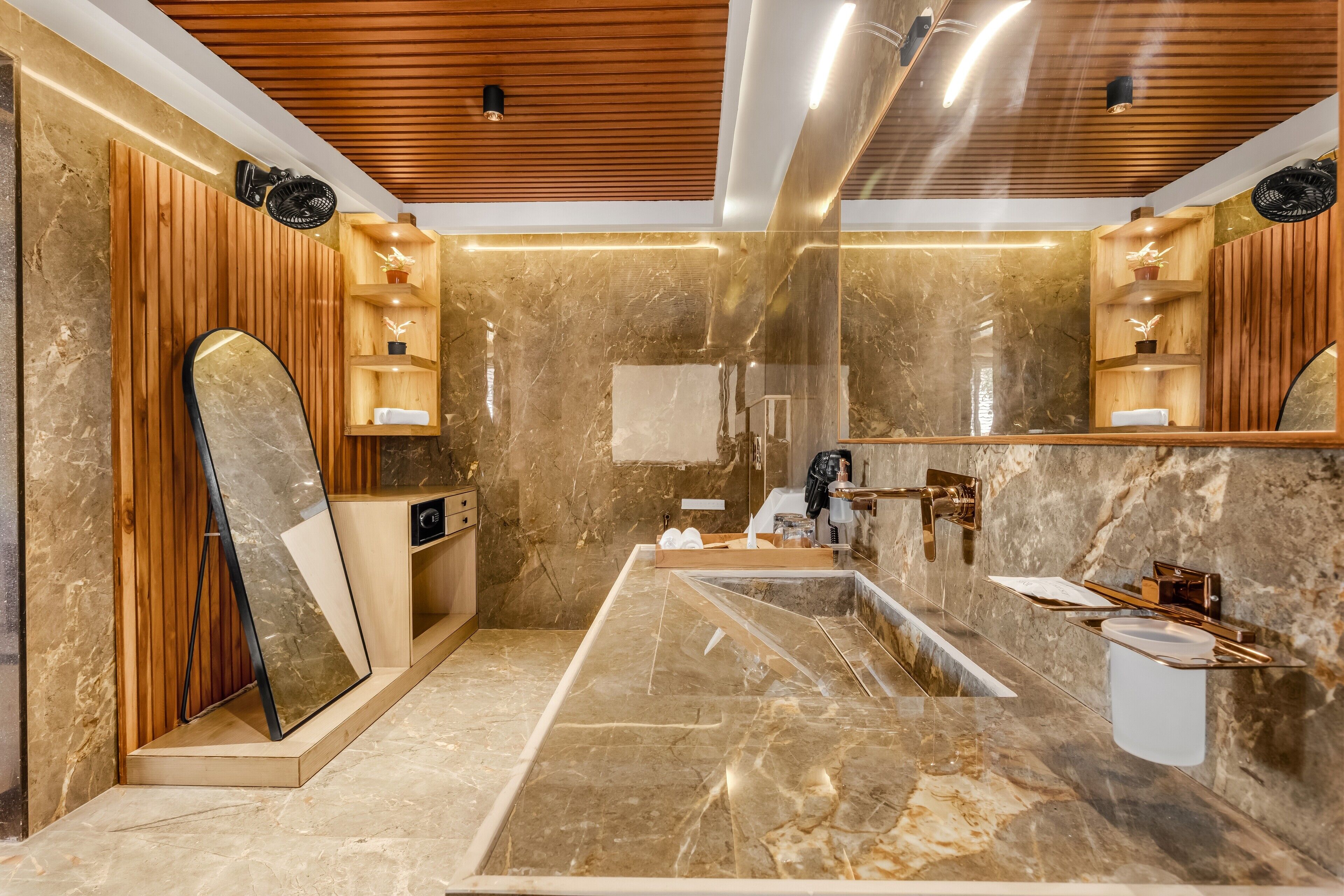 A modern bathroom with a large mirror, marble flooring, wooden paneling, and built-in shelves.