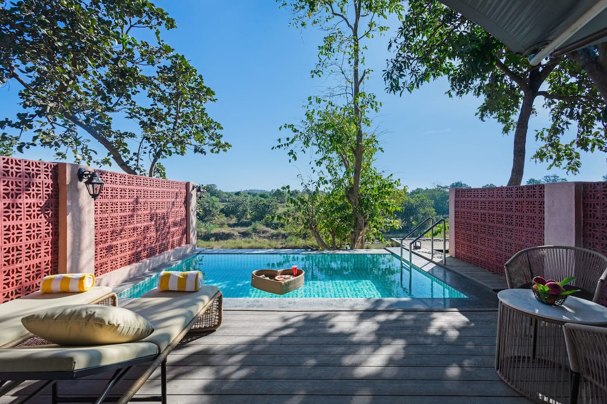 An outdoor swimming pool with lounge chairs and a table, surrounded by a wooden deck and red lattice walls.