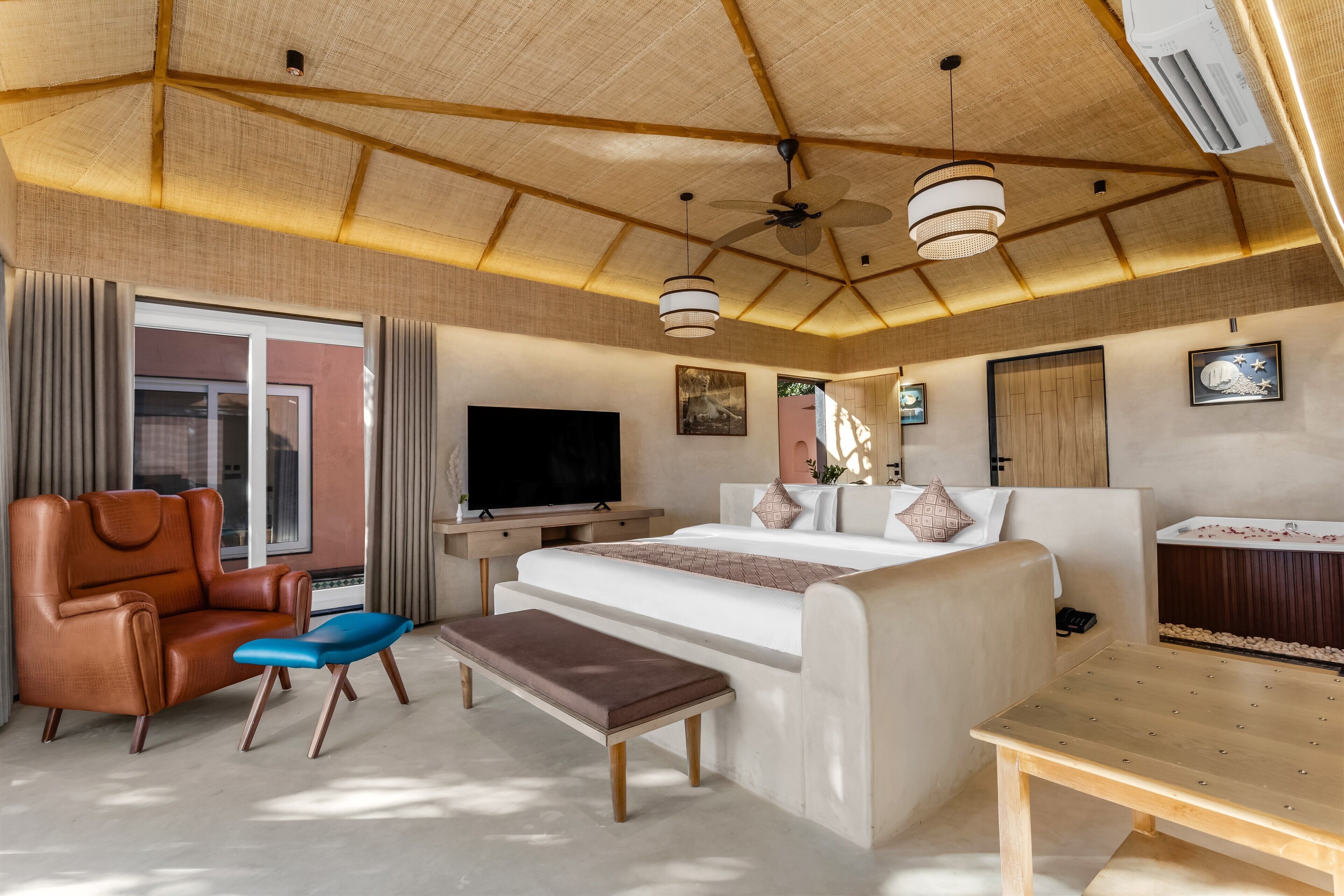 A modern hotel room with a large bed, a sofa, a desk, a TV, and a ceiling fan.