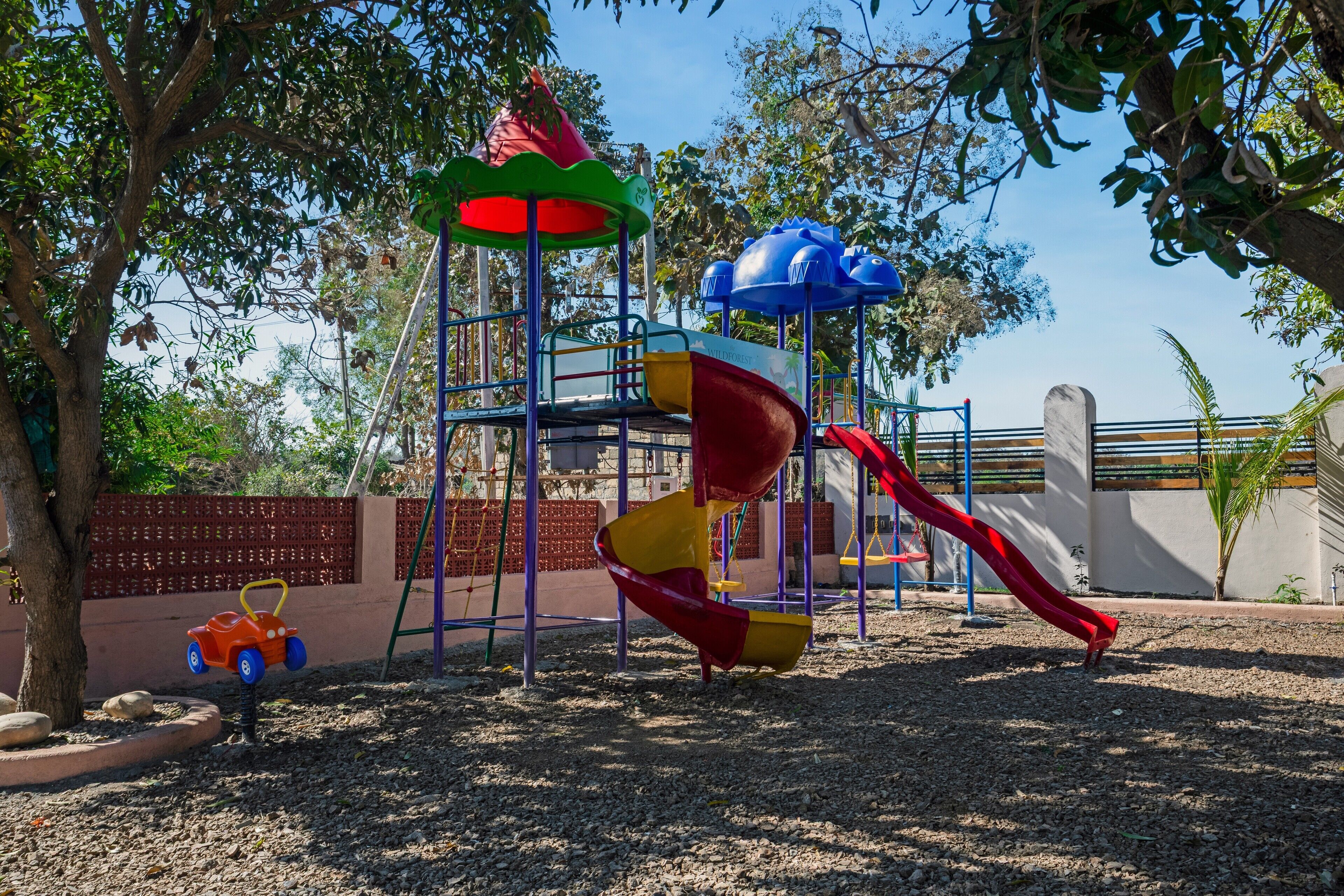 Un parque infantil con un tobogán, estructuras para escalar y un pequeño coche de juguete naranja.