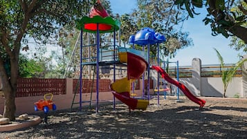 Un parque infantil con un tobogán, estructuras para escalar y un pequeño coche de juguete naranja.