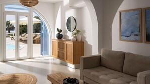 Ein modernes Wohnzimmer mit einer Couch, einem Holzschrank und einem großen Fenster mit Blick auf einen Poolbereich.