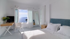 Ein modernes Hotelzimmer mit einem Bett, einem Schreibtisch mit Computer, einem Sessel und Blick aufs Meer.