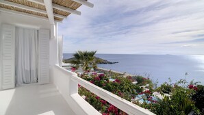 Ein Balkon mit weißen Geländern, Blick auf das Meer und ein kleiner Garten mit rosa Blumen.