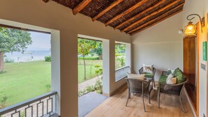 Un balcone con vista su una zona verde e un corpo d'acqua, arredi in vimini e un soffitto in legno.