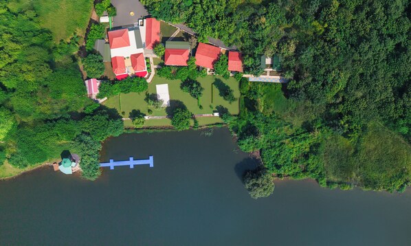 An aerial view of a lakeside property with multiple buildings, a dock, and surrounding greenery. - The Forest Chapter By Sayaji Madhai (Sarangpur)