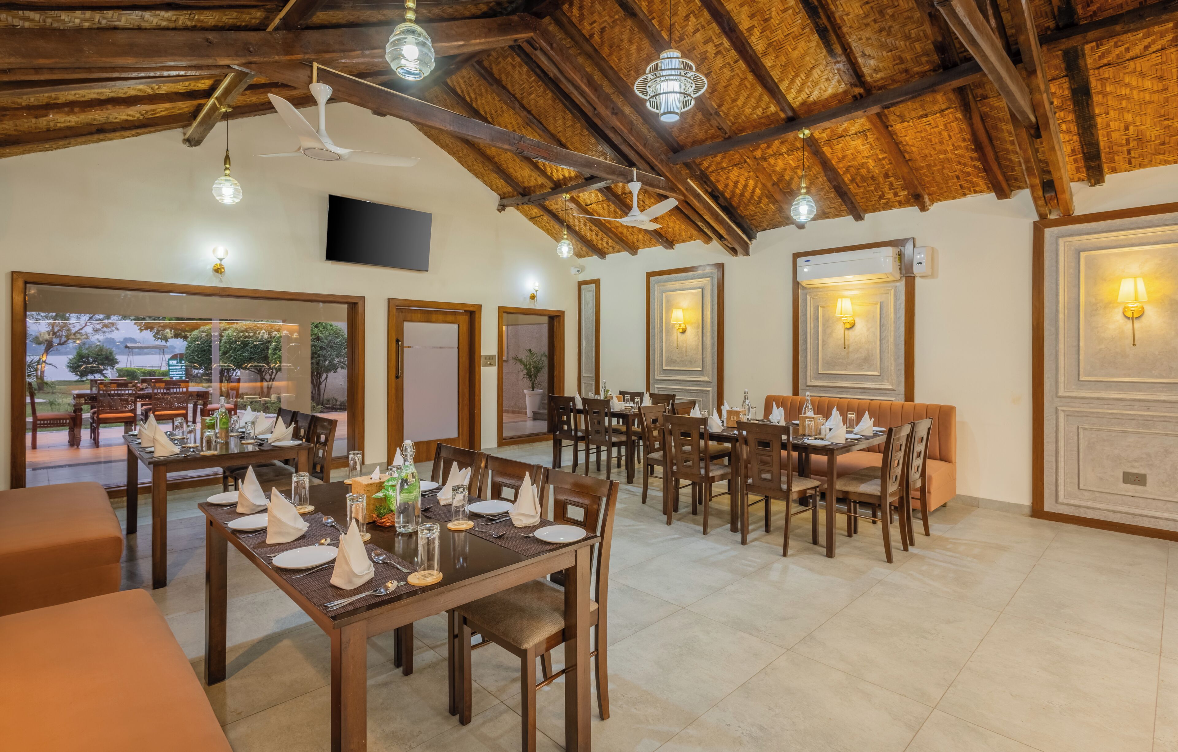 A dining area with wooden tables and chairs, ceiling fans, and wall-mounted lights.