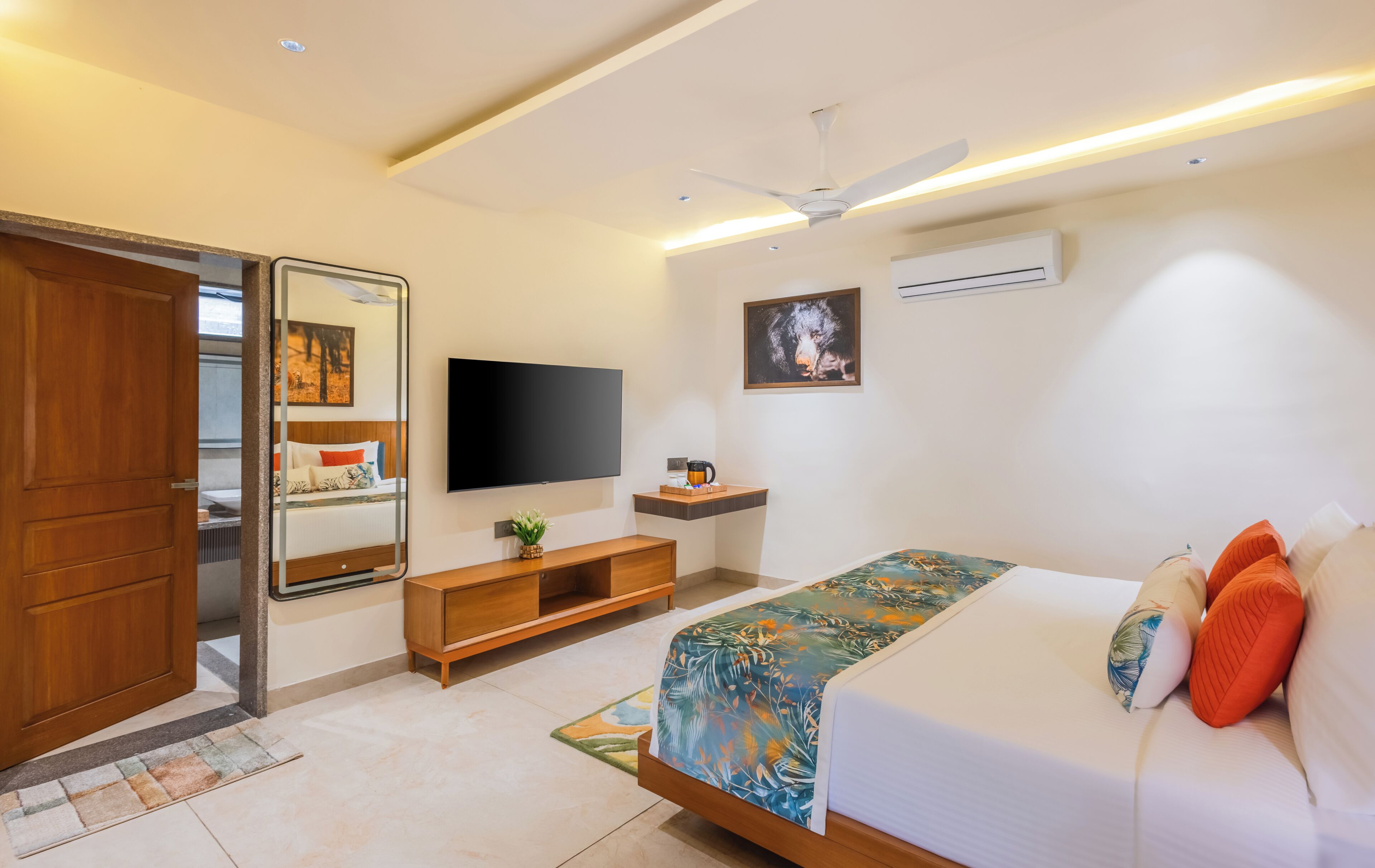 A modern hotel room with a bed, a flat-screen TV, a ceiling fan, an air conditioning unit, and a wooden door.