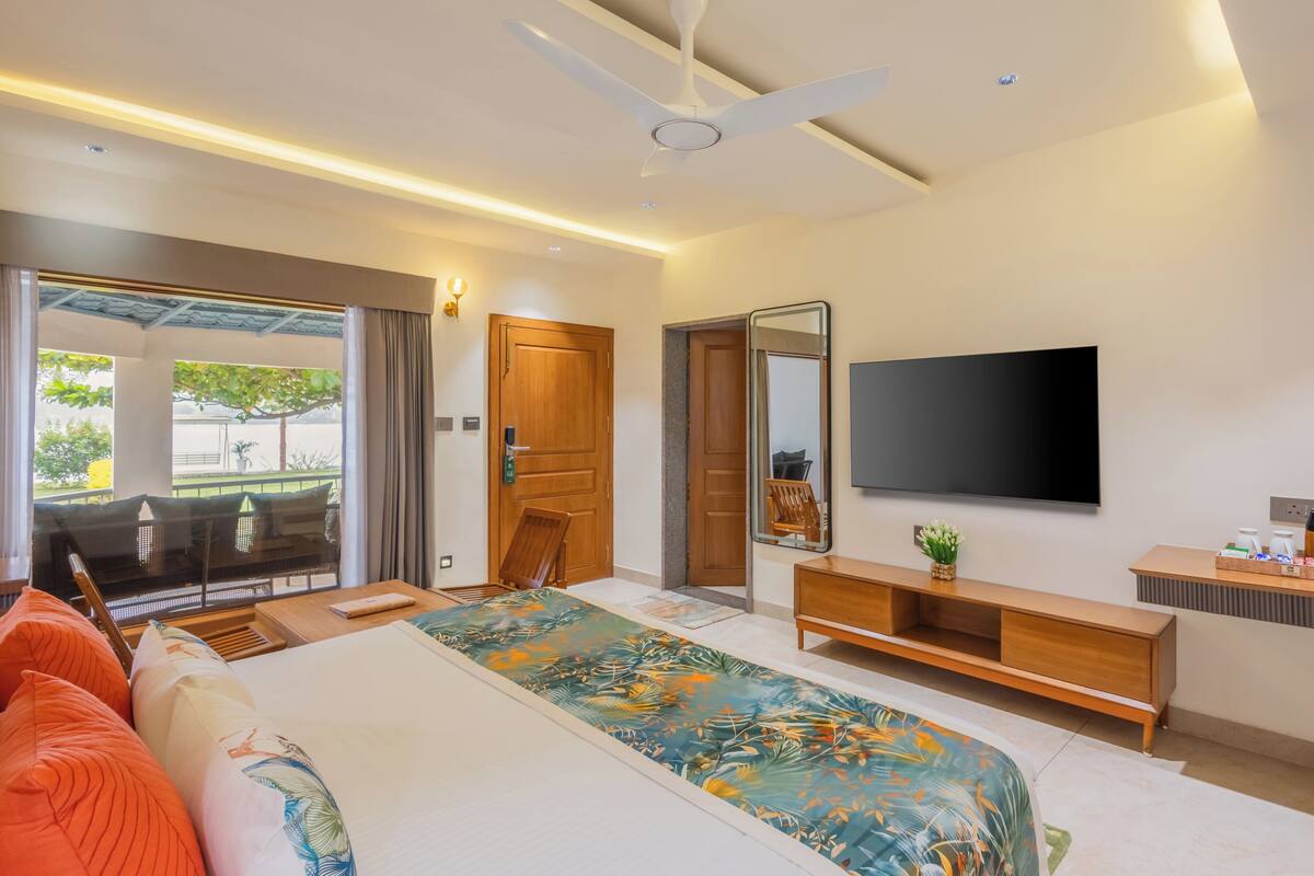 A modern hotel room with a bed, a TV, a wooden dresser, a mirror, and a ceiling fan.