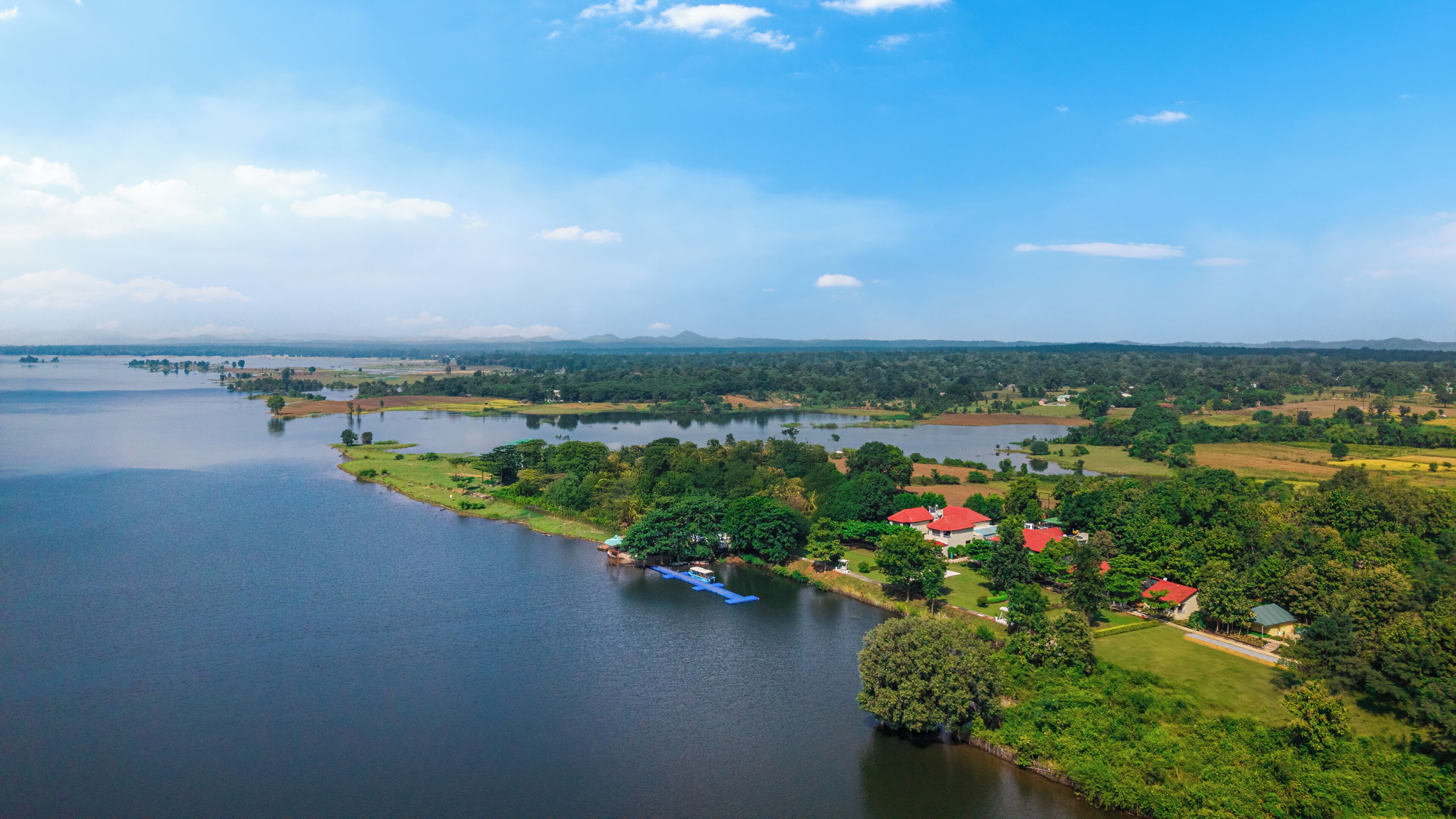 Uma propriedade à beira de um lago, com um edifício de telhado vermelho, um cais e vegetação ao redor.